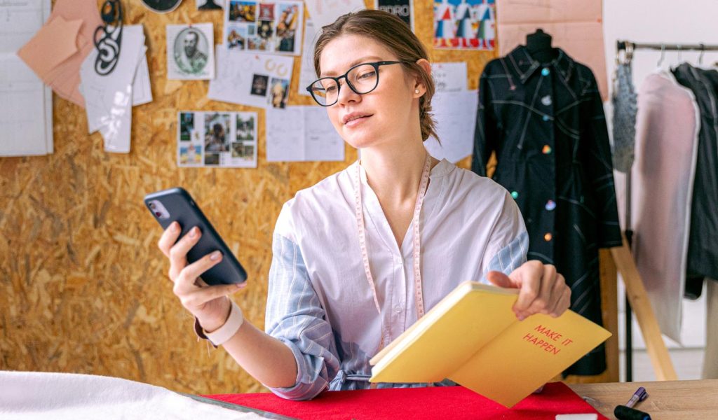 Person looking at phone with book in hand, getting inspiration and ideas to plan a notebook or journal